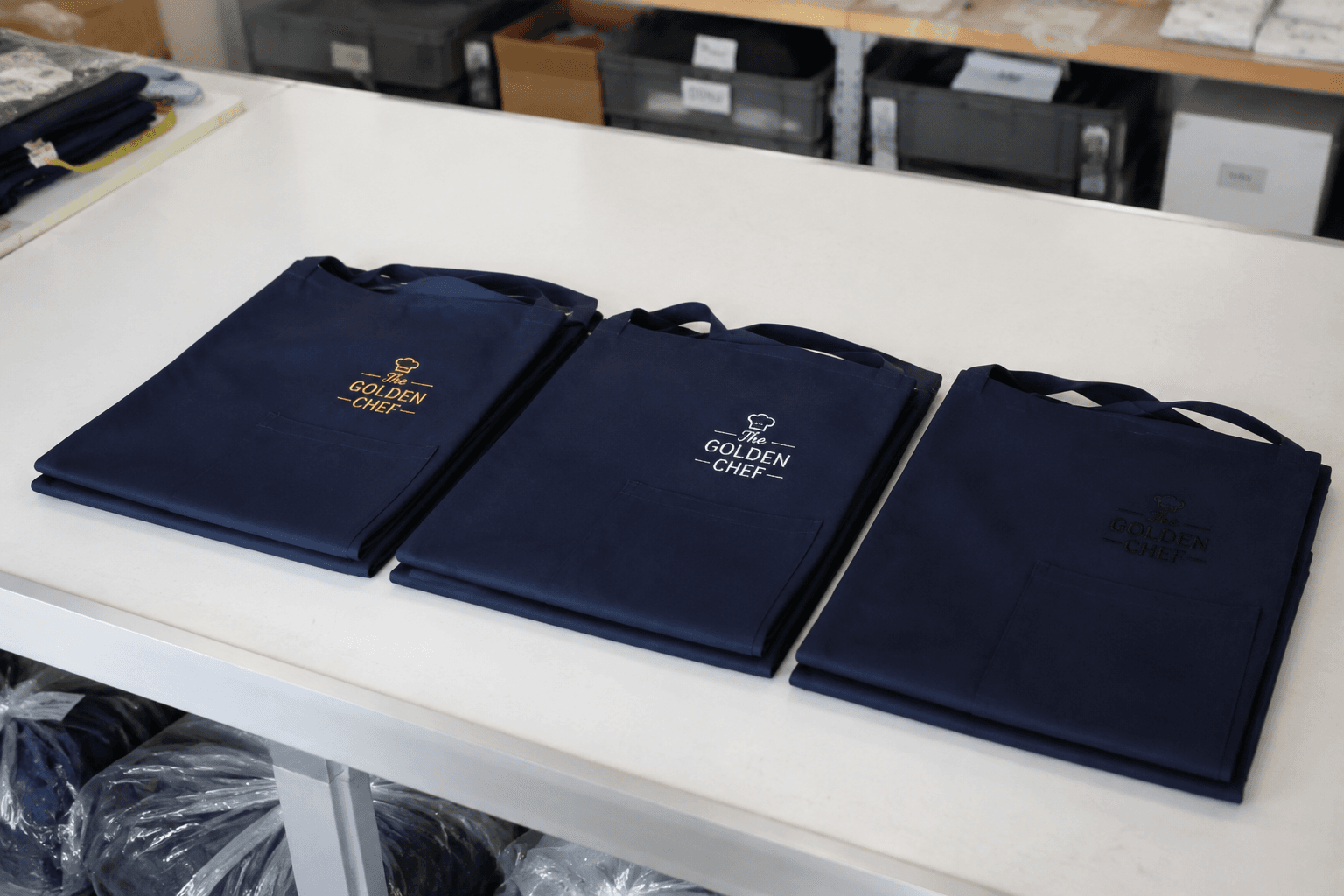 neatly folded navy lounge aprons with discreet embroidered logo samples in a factory inspection area