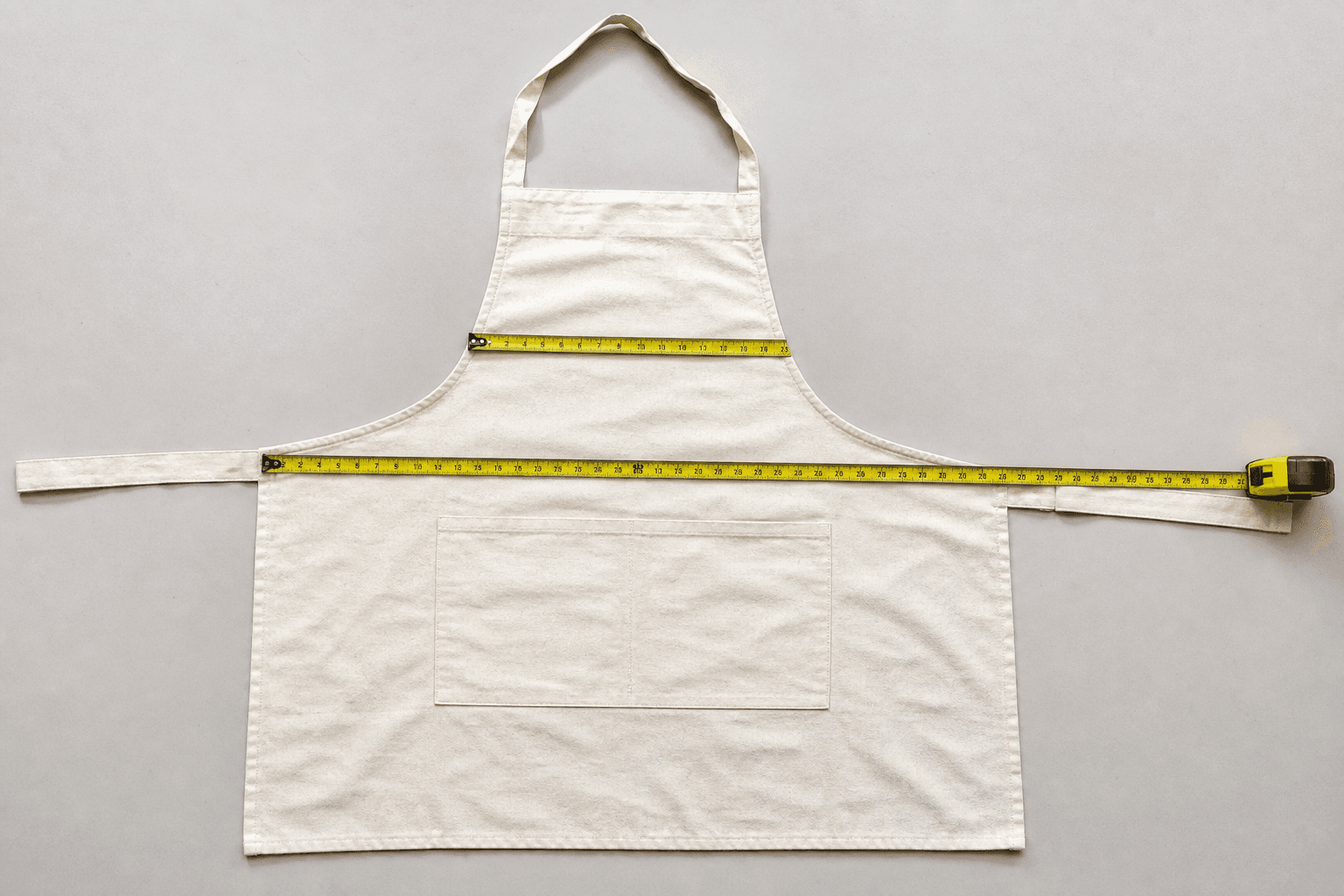 An apron laid flat with a measuring tape across the bib and waist