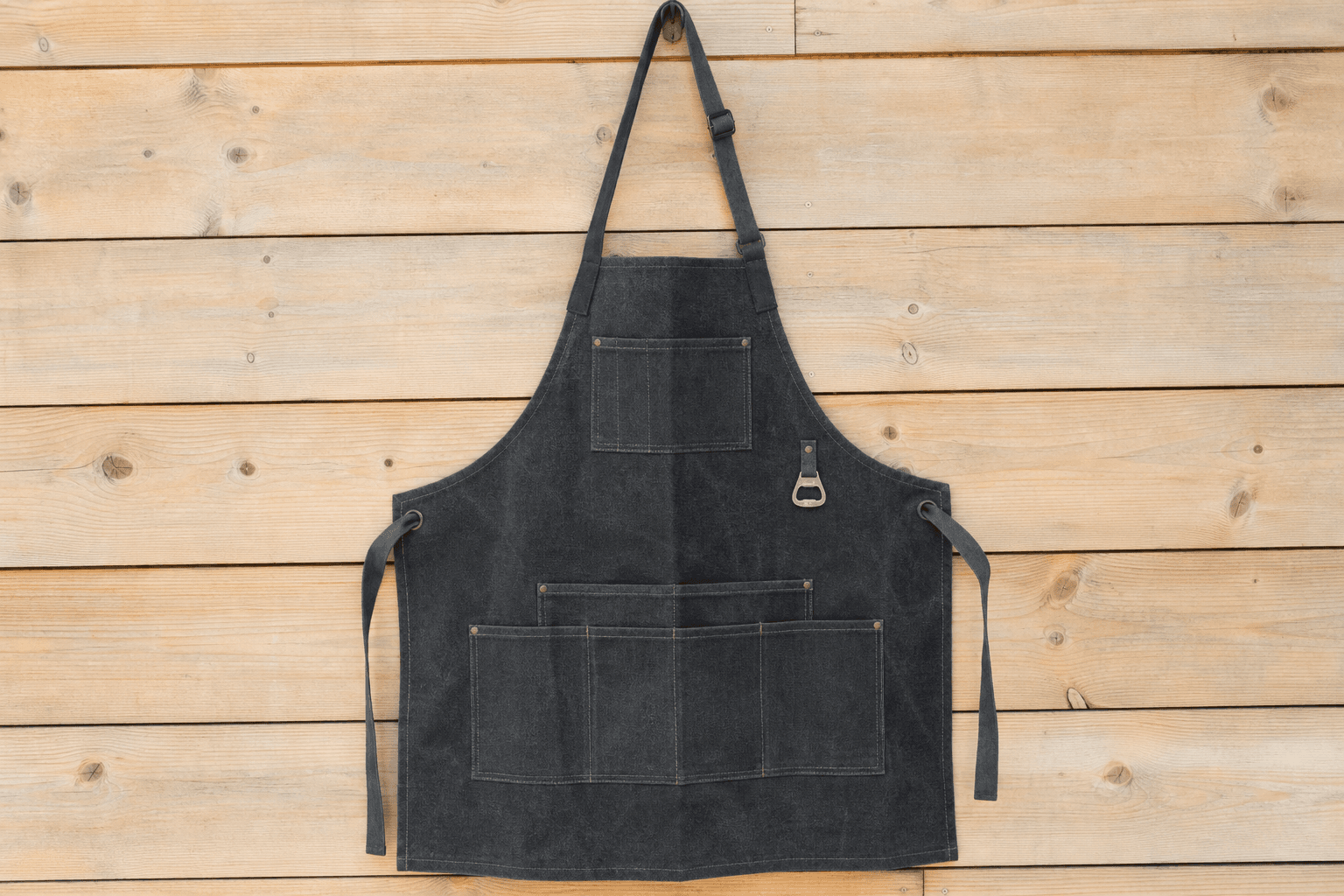 A heavyweight canvas grilling apron with tool pockets on a wooden wall