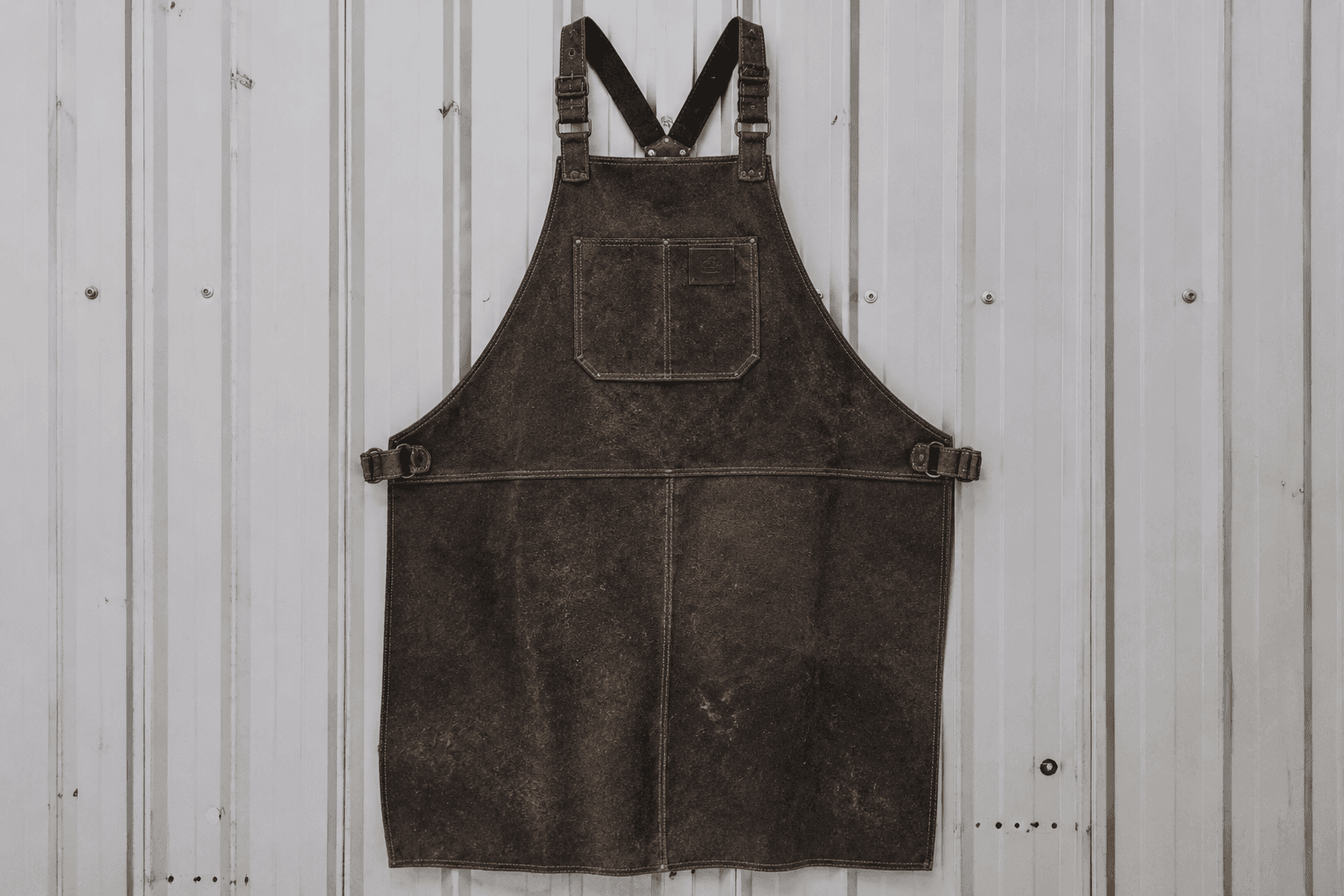 A heavy split-leather blacksmith apron hanging on a workshop wall