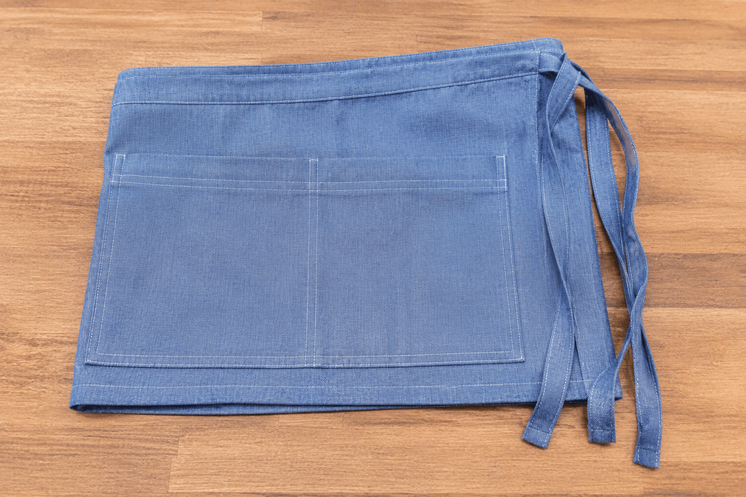 A pale indigo chambray half apron folded on a wooden counter