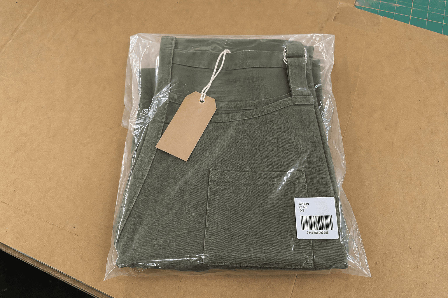 A folded apron with a kraft hangtag and polybag on a packing table