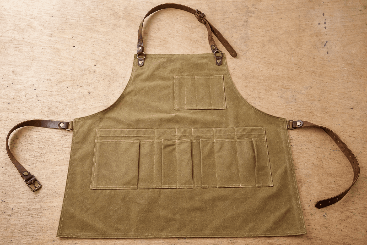 A waxed-canvas florist apron with tool pockets on a wooden bench