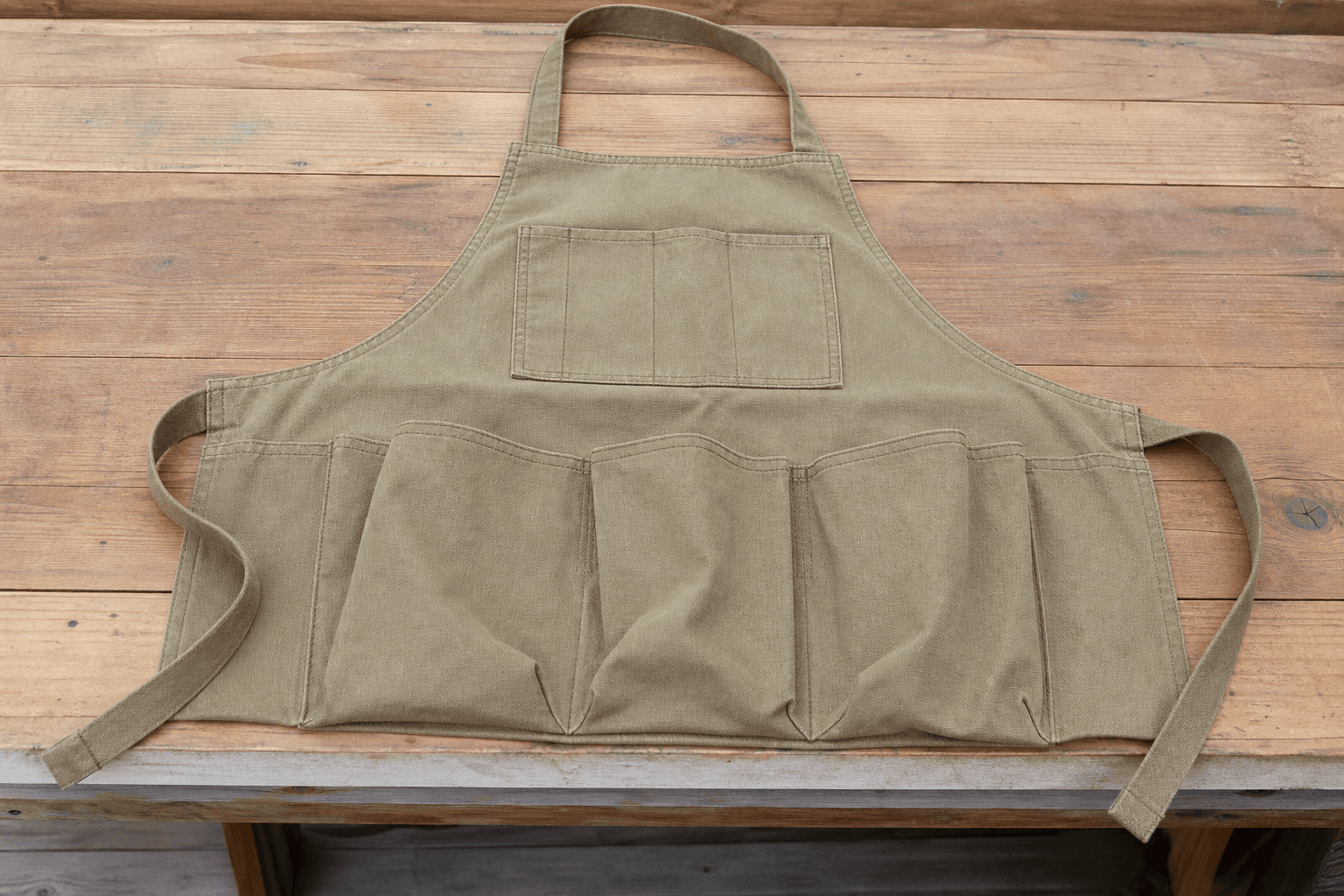 A canvas gardening apron with deep tool pockets on a potting bench