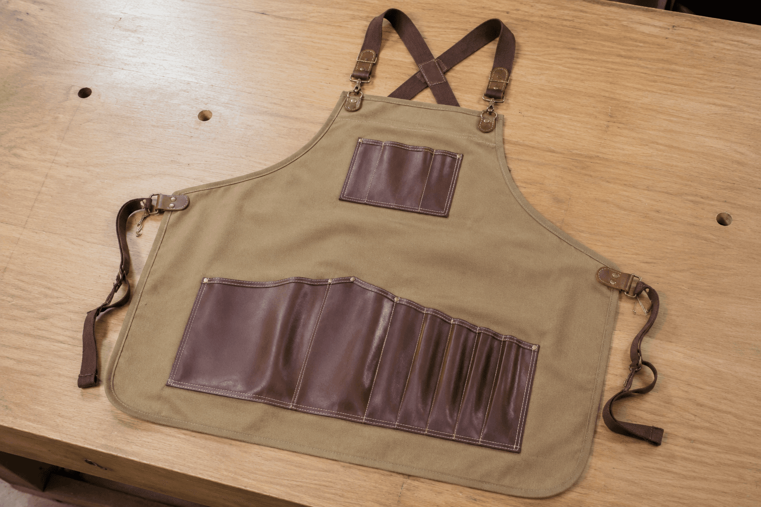 A heavy canvas-and-leather craft apron with tool pockets on a bench