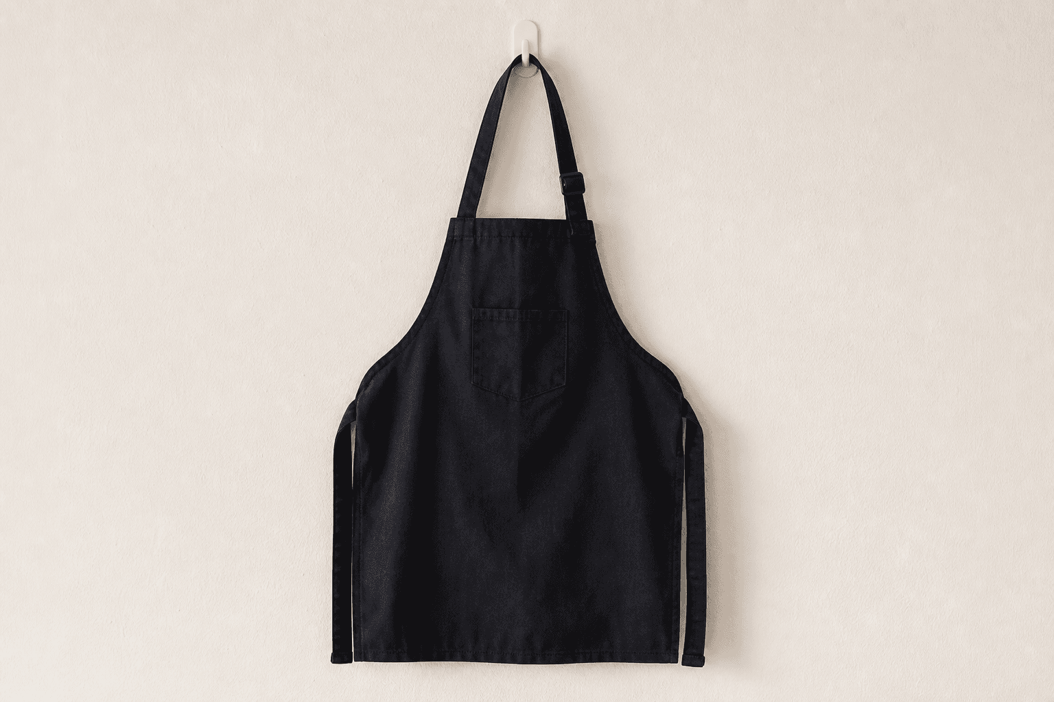 A short black esthetician apron with a chest pocket on a wall hook