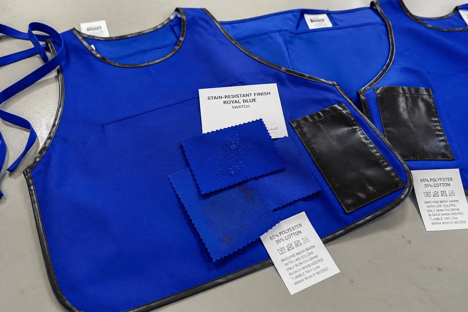royal blue cafeteria apron samples with plastic trim and care labels on an inspection table