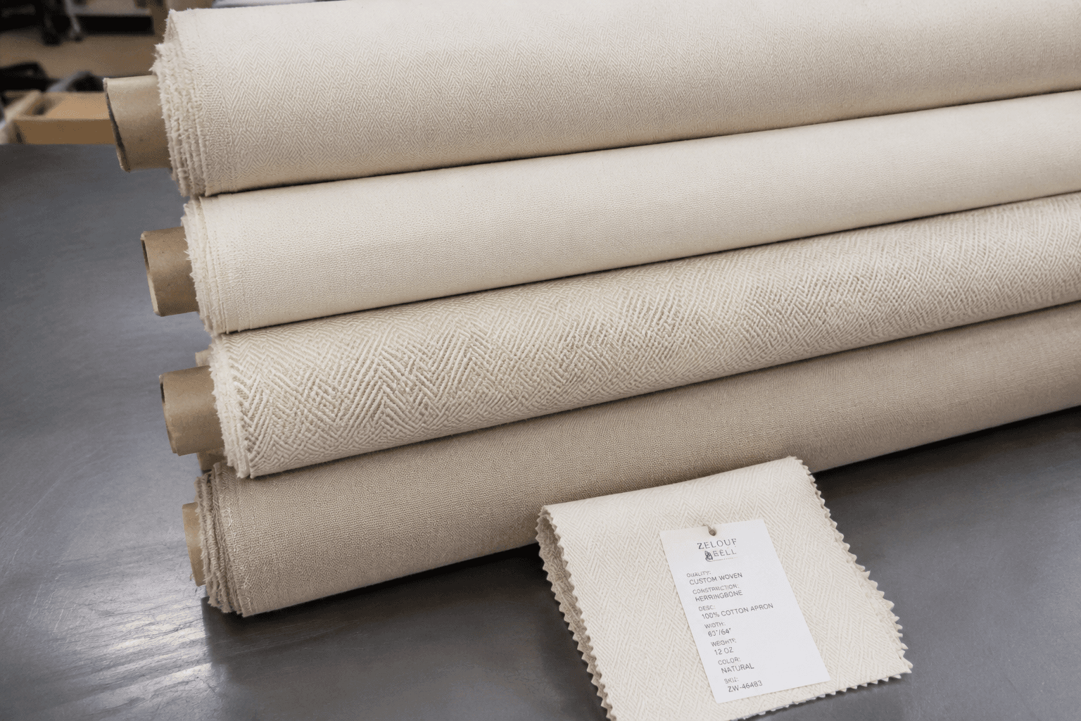 Rolls of stocked apron fabric beside a small custom-woven swatch on a factory table