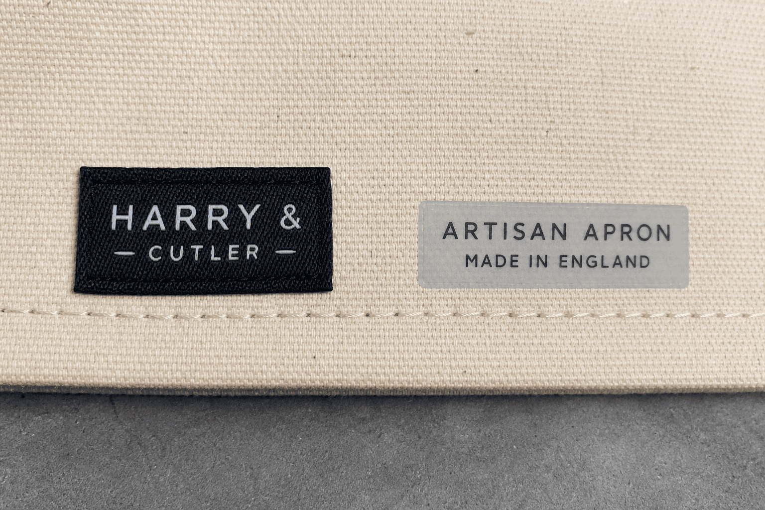 A woven brand label stitched to an apron hem beside a heat-transfer label