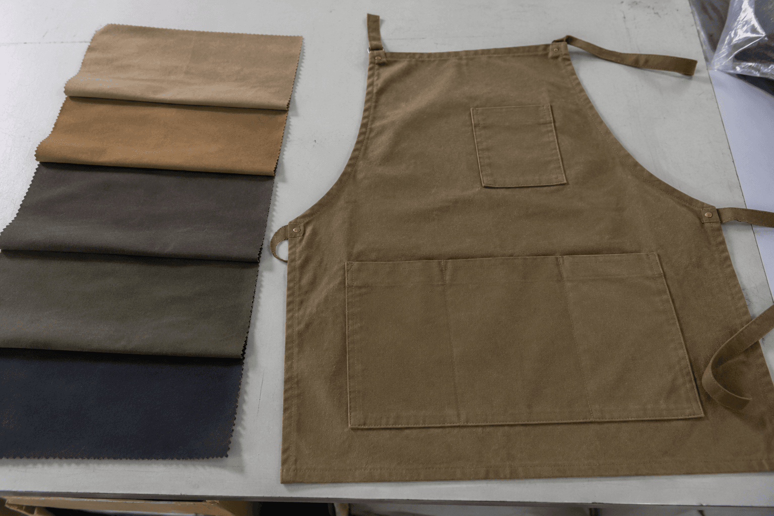 Realistic photo of moleskin apron fabric swatches and a finished apron panel laid flat in a factory sampling area, no people.